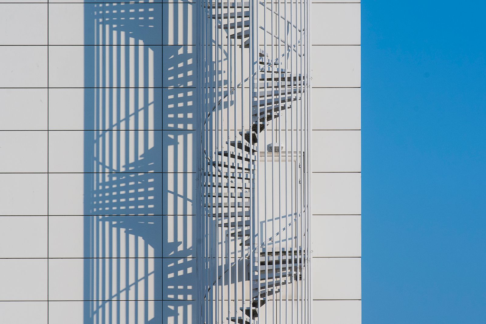 A spiral staircase casts a geometric shadow on a building facade